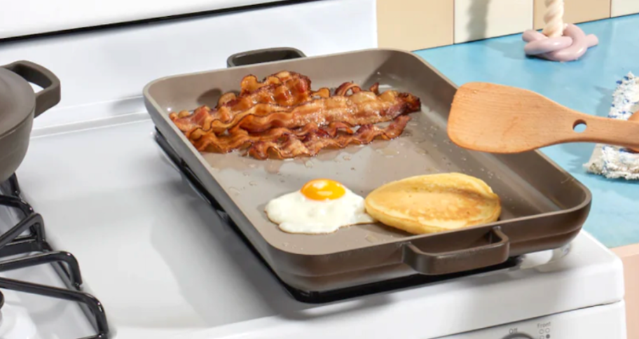 gray griddle with eggs, bacon and toast cooking 