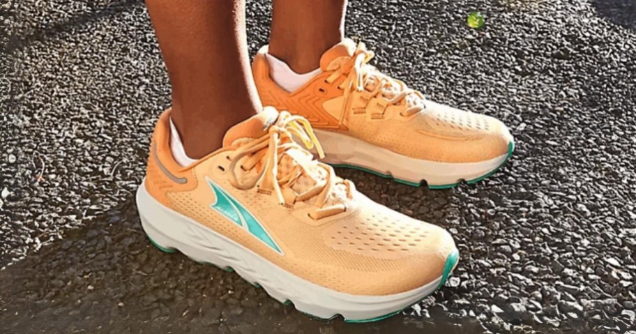 women's feet wearing light orange and white Altra running shoes standing on a road