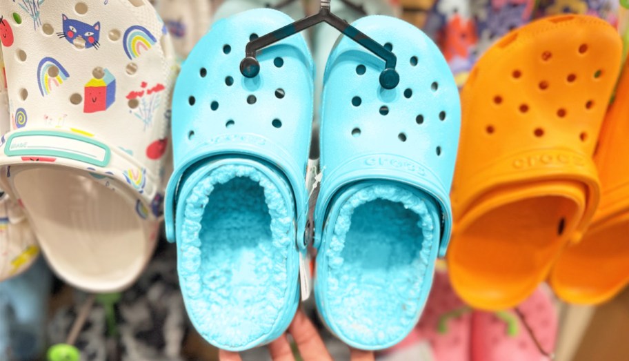 hand touching a pair of blue lined crocs hanging from store display