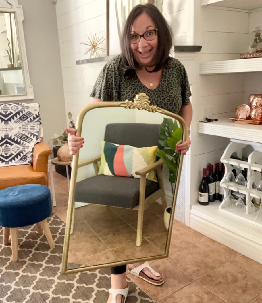 woman holding gold mirror in living room