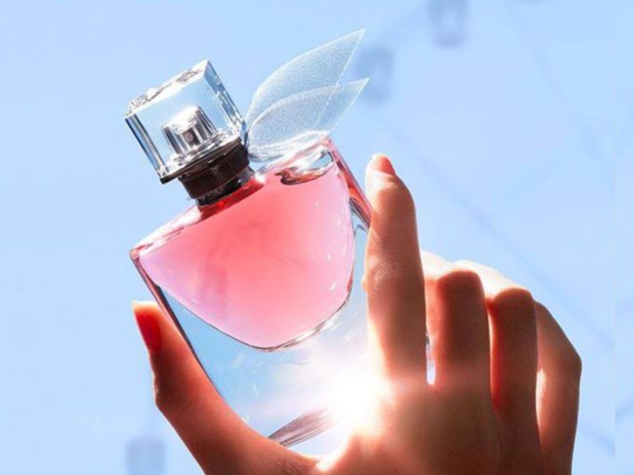 hand holding perfume bottle in sky