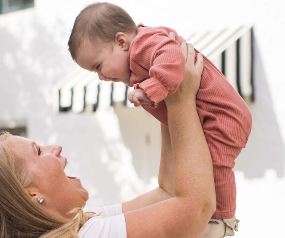 mom holding baby in air in jumpsuit