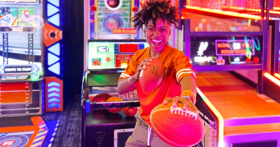 woman holding 2 footballs in front of Dave & Busters game