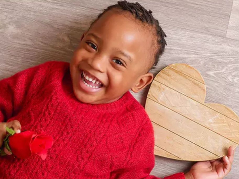 Little boy holding a rose with a wooden heart cutout next to him