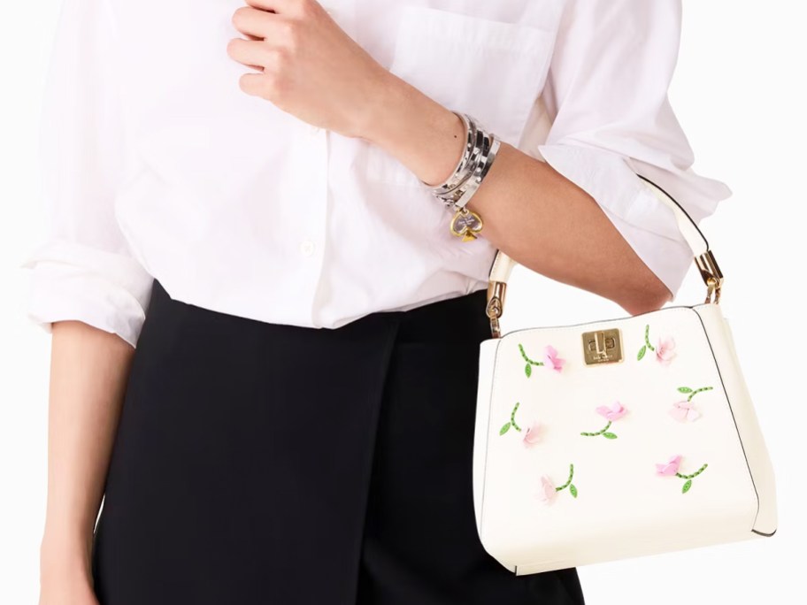 woman in a white top and black pants holding white floral print purse