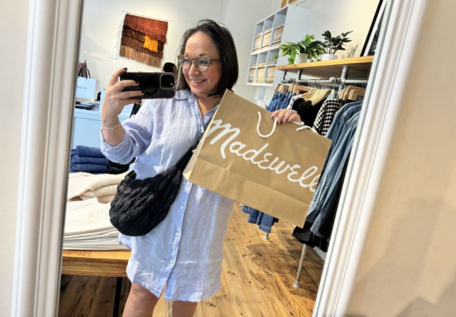 woman holding a madewell shopping bag taking a selfie in store