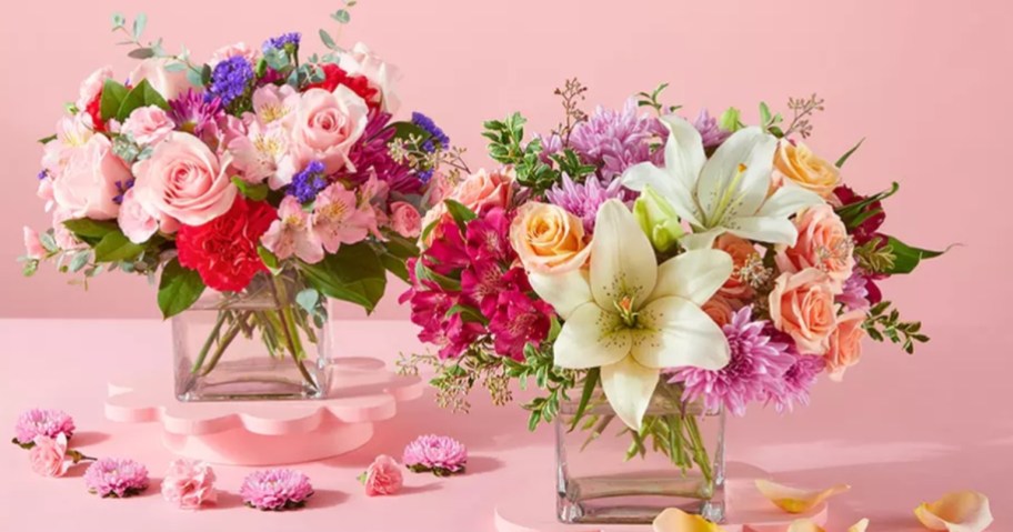 two small vases of flowers, one has white lilies and red roses and pink and purple flowers, the other has pink and red roses and pink and purple and white flowers 