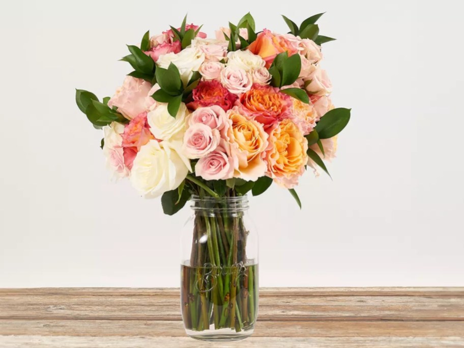 a vase with pink, peach, red and white roses and flowers