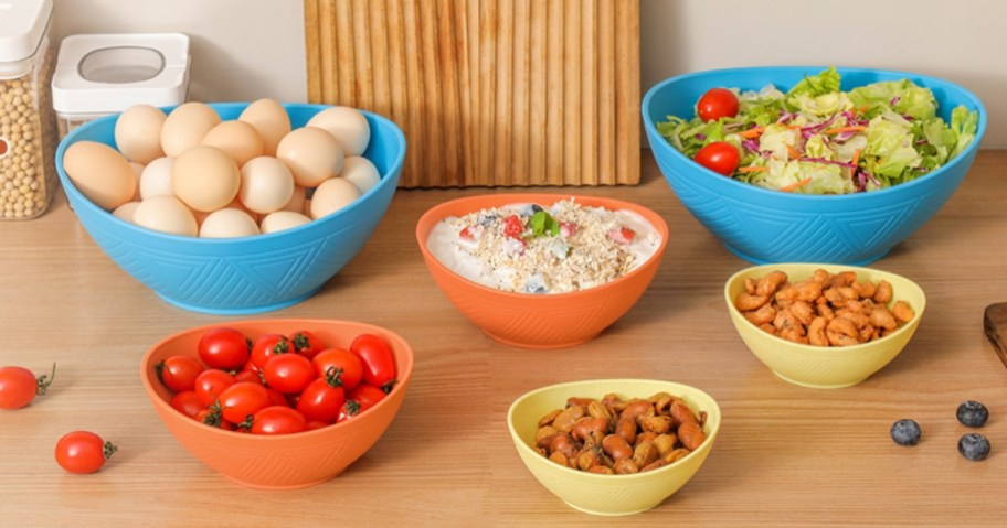 a set of 6 colorful mixing bowls in various sizes on a counter, each bowl has a different food item in it