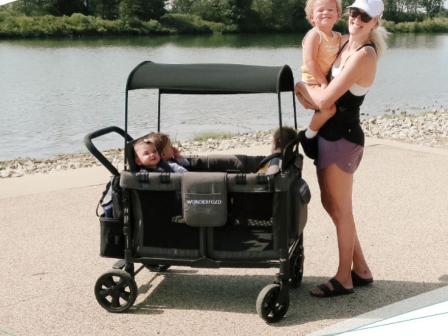 mom holding child with three more kids in a wagon on the beach 