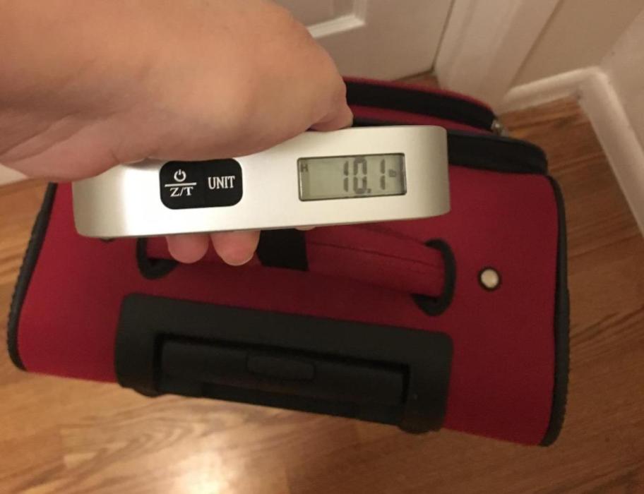 hand holding luggage scale with red suitcase