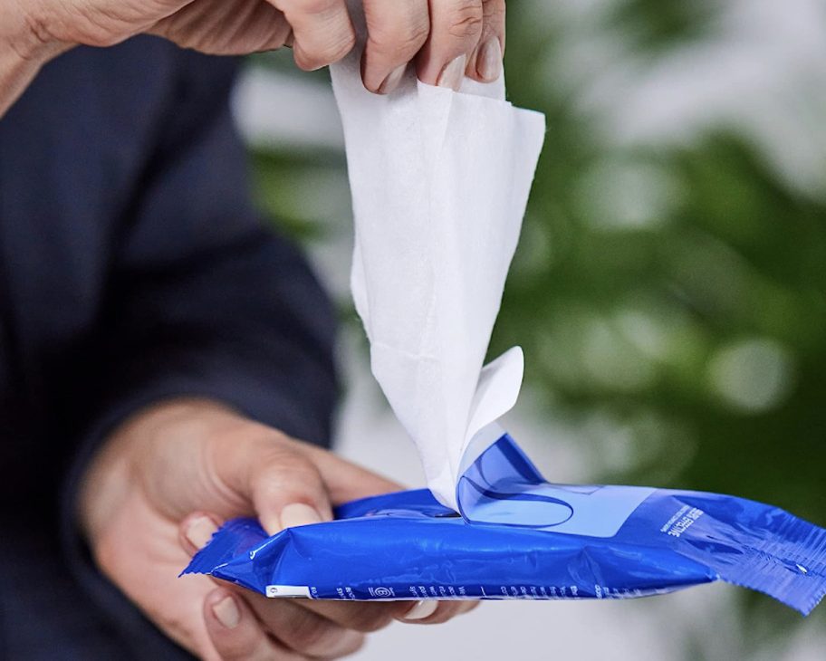 hand pulling out hand sanitizing wipes from travel products package