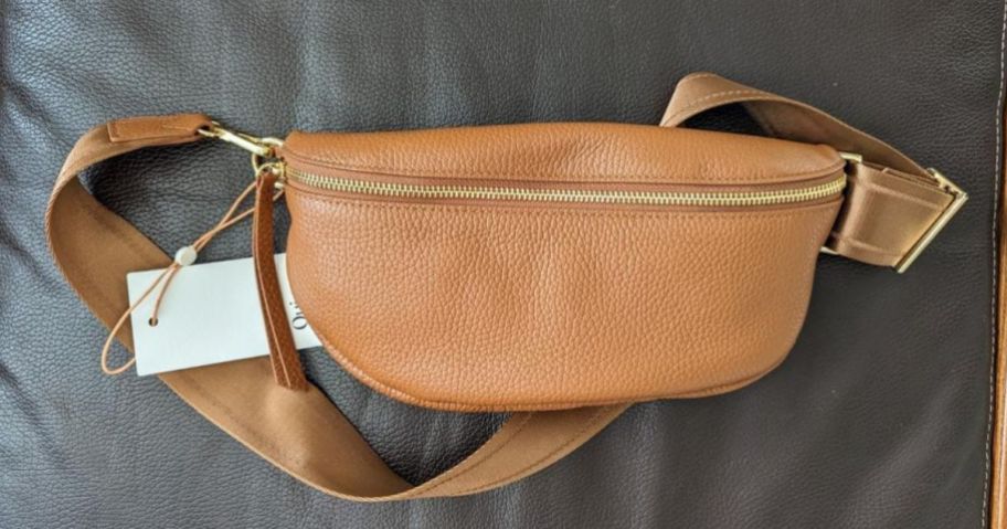 A Quince Italian Pebbled Leather Sling Bag in Cognac on a bed