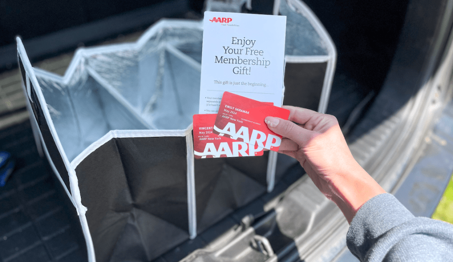 hand holding up AARP cards next to a black and silver trunk organizer