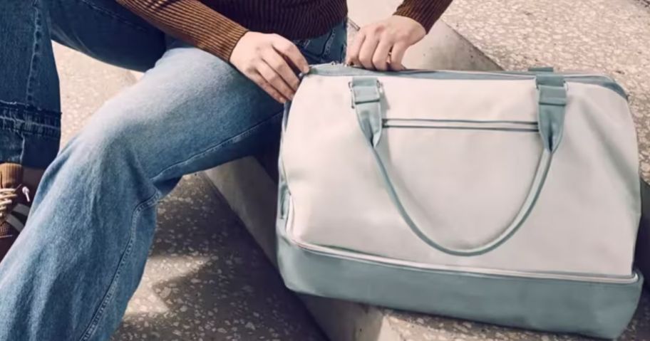 Woman sitting unzipping a blue and white DSW tote bag