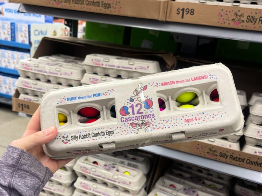 Woman holding cardboard package of Easter confetti eggs, inside Walmart store