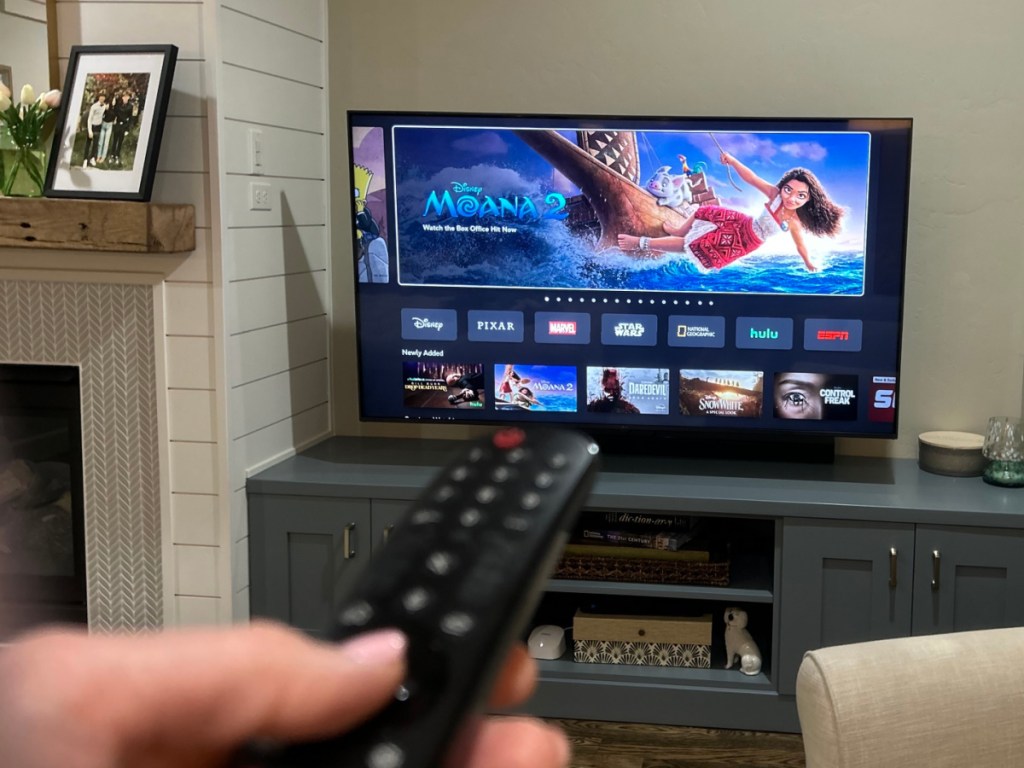 Person aiming TV remote control at TV with Disney's Moana 2 on screen