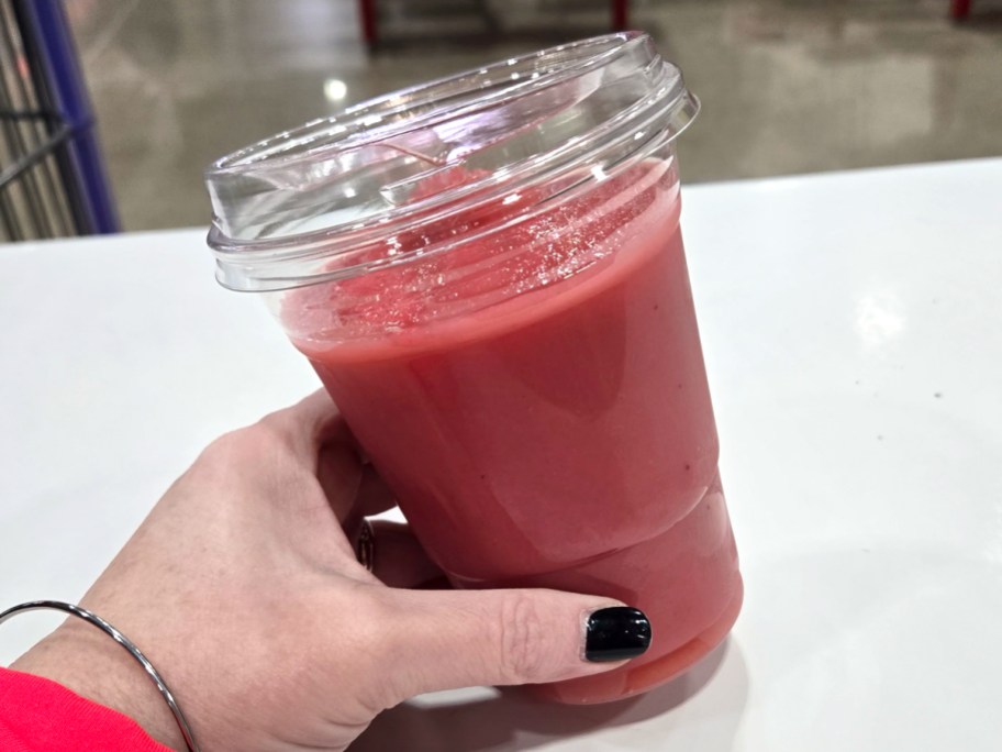 Costco Strawberry Banana Smoothie being held by a woman at a table in Costco