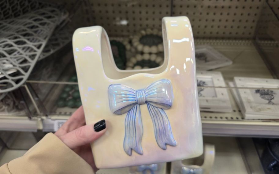 a womans hand holding a square vase with a blue bow on it 