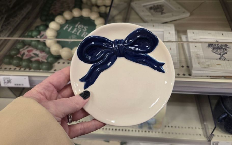 a womans hand holding a round trinket dish with a blue bow on it 