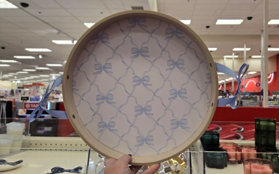 a womans hand holding a round wooden tray with a blue bow print 