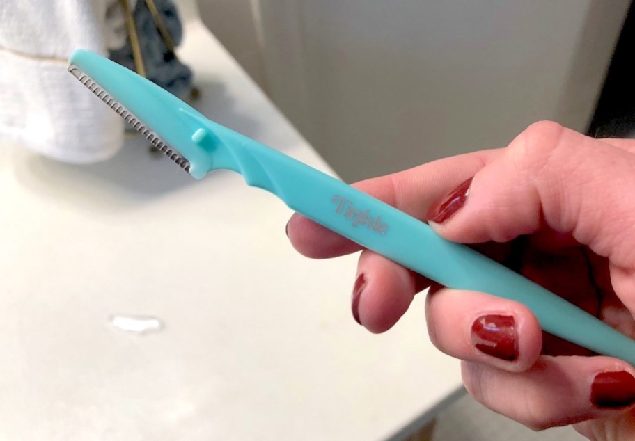 hand holding a blue tinkle razor in bathroom