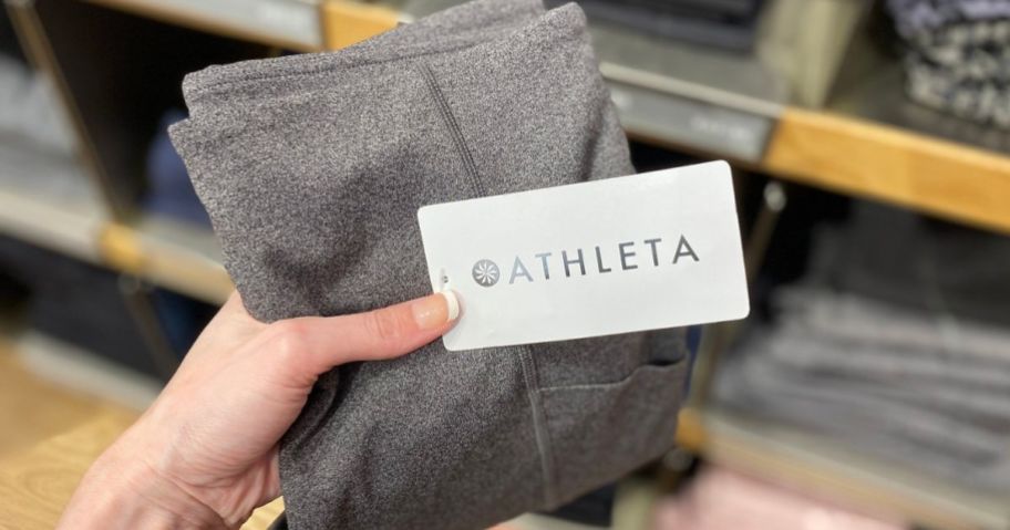 Hand holding up a pair of brand new Athleta Leggings with the tag on them