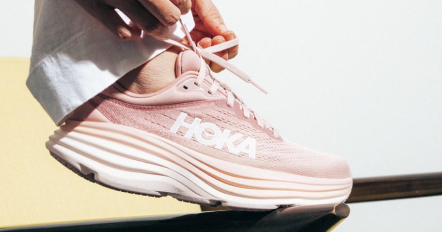 woman tying laces on pink hoka shoe