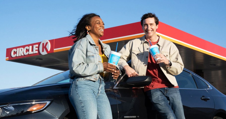 two people holding drinks and leaning against car at Circle K gas station 