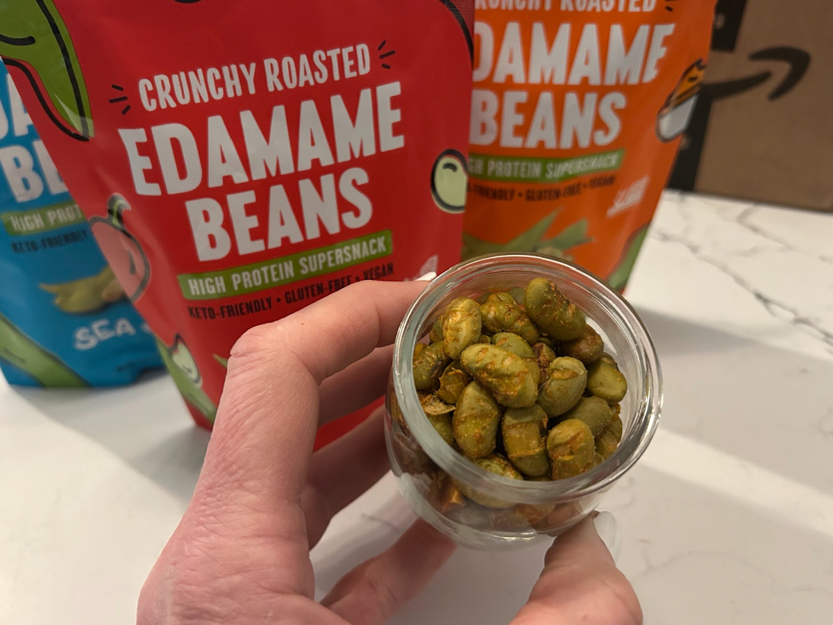 Small glass jar of roasted edamame beans in front of several different snack bags of more edamame beans