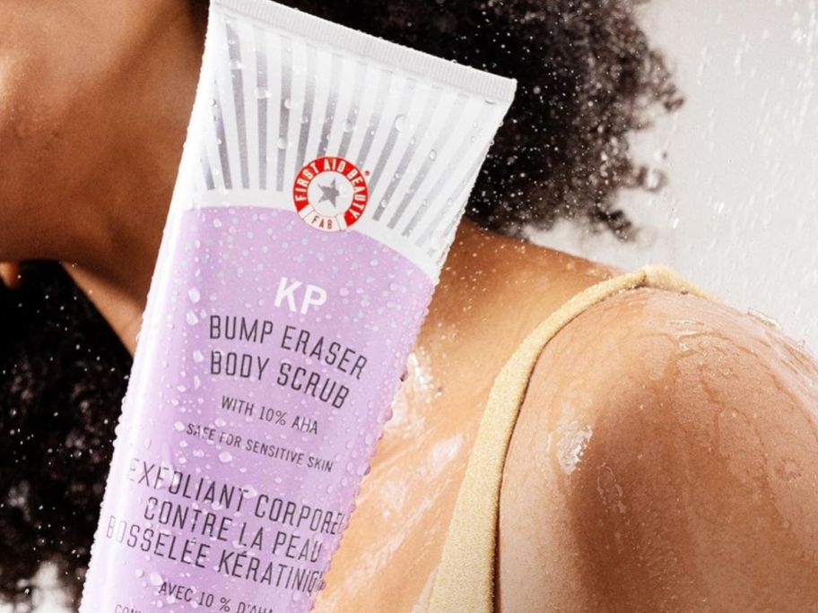 Woman holding a tube of First Aid Beauty KP Bump Eraser Body Scrub