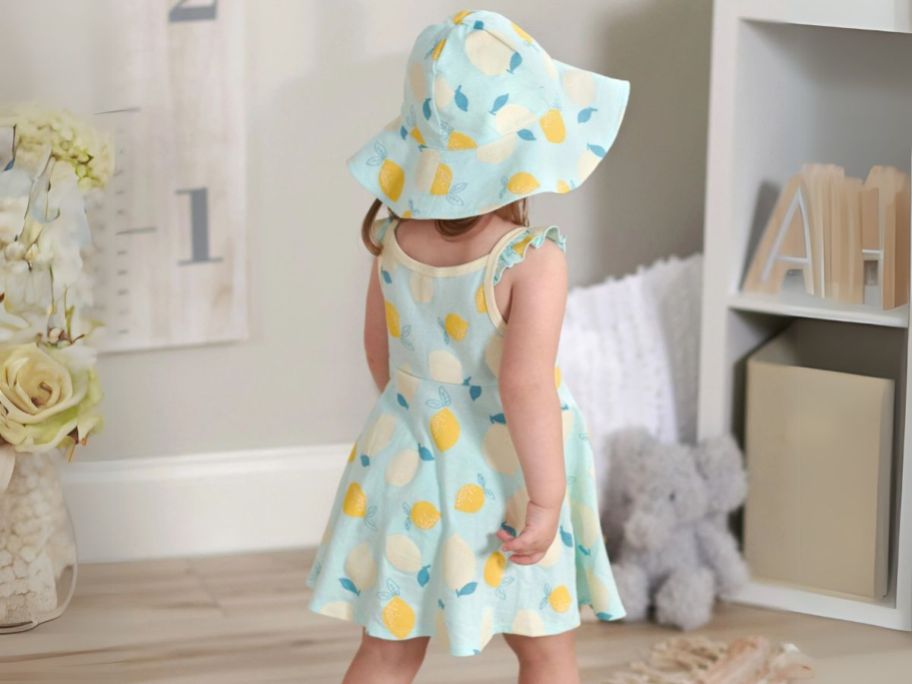 girl wearing Gerber 3-Piece Baby & Toddler Girls' Dress, Diaper Cover & Reversible Sun Hat Set in bedroom