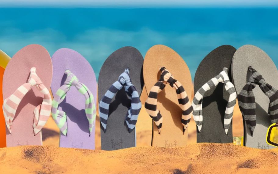 womens flip flops in assorted colors, sticking up out of the sand on a beach