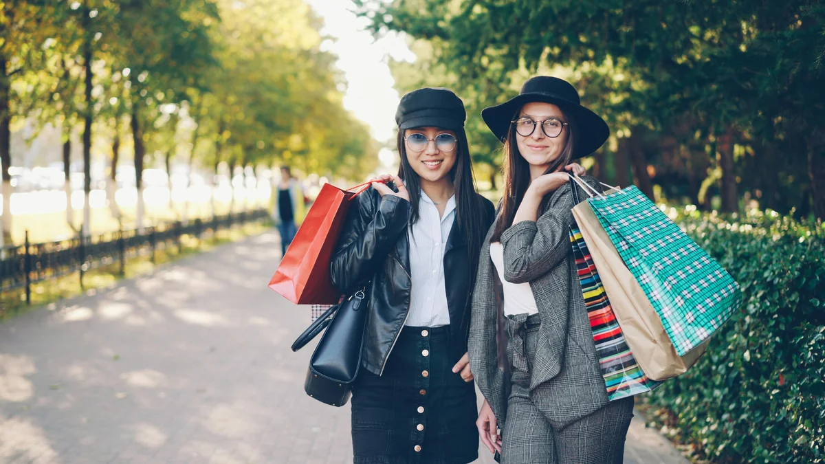 Portrait of happy girls shopaholics standing outdoors with bright bags, looking at camera and smiling touching hair. Shopping, people and modern youth lifestyle concept. - comparison of best coupon sites for fashion