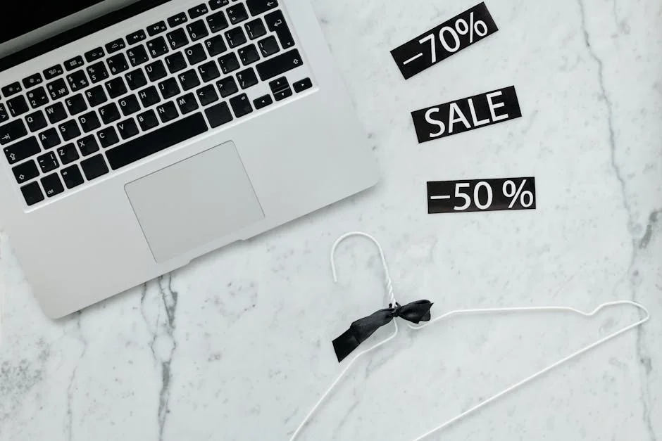 Flat lay of a laptop, hanger, and sale stickers on a marble desk, ideal for Black Friday themes. - limited time luxury fashion sales online