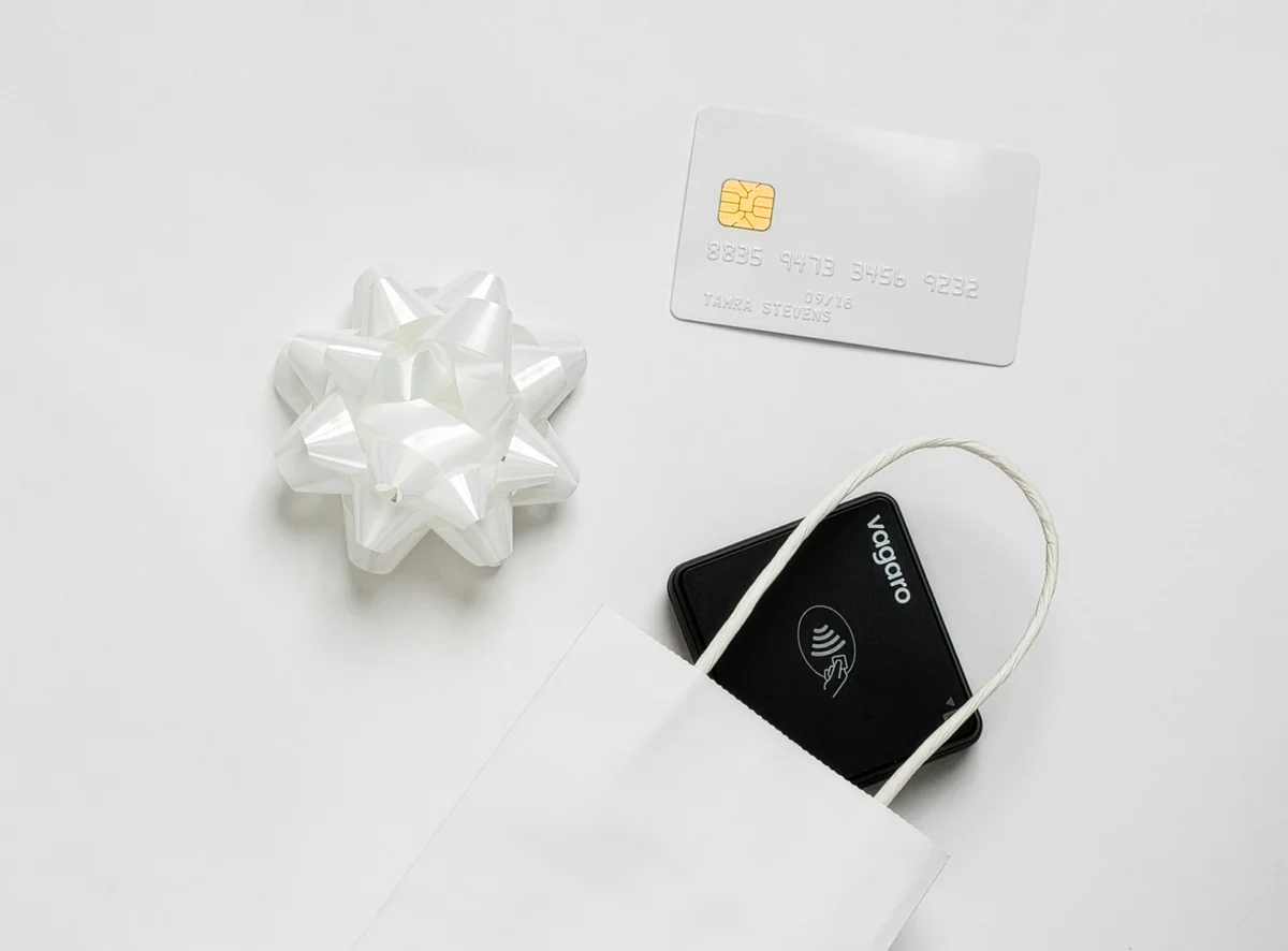 The Vagaro Credit Card Reader coming out of a gift bag sits next to a present bow and credit card, ready to checkout customers for the holidays. - redeemable gift card codes for online retailers