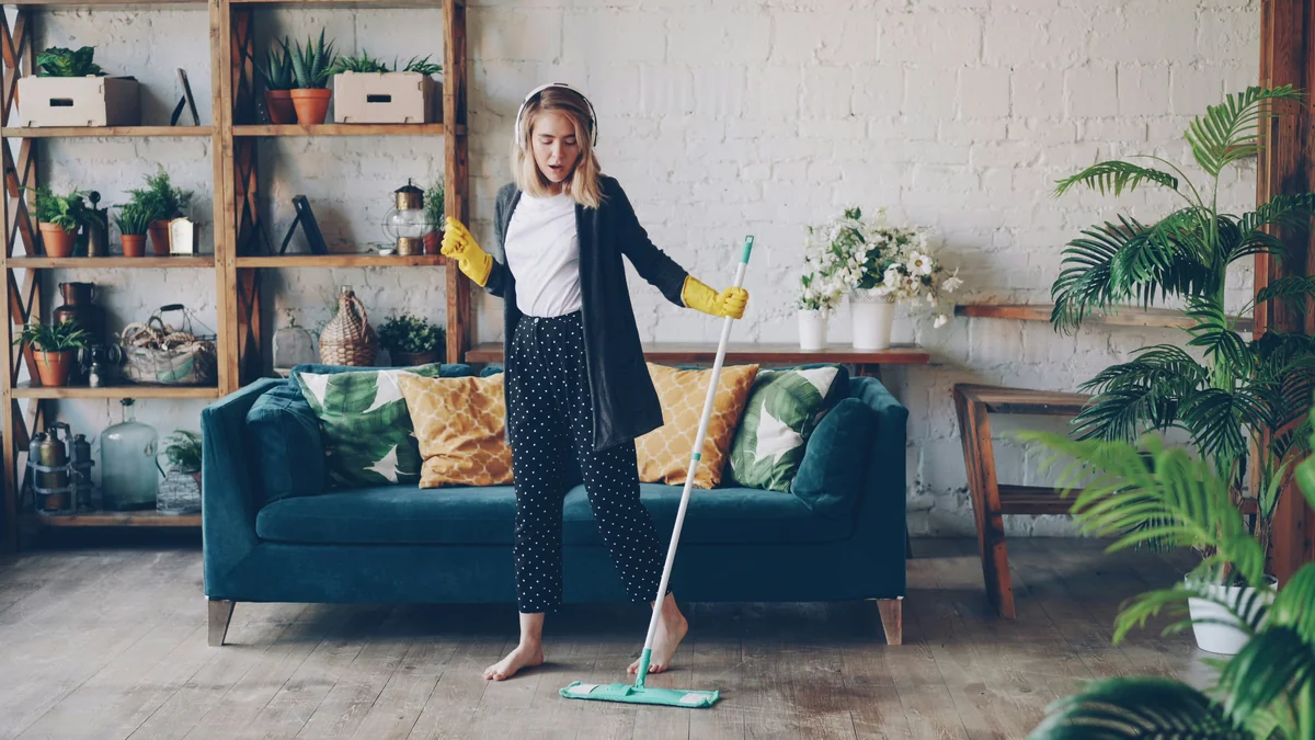 Attractive girl in headphones is listening to music and dancing wih mop during domestic work, she is mopping floor at home and having fun. Women, joy and modern houses concept. - spring cleaning supply coupons and household deals