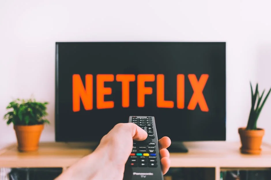 A hand holding a TV remote in front of a screen with Netflix, perfect for streaming and movie night themes. - subscription renewal discounts for streaming services
