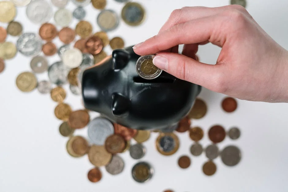 Close-up of a hand inserting a coin into a black piggy bank with scattered coins on a white background. - piggy bank money - How to use digital coupons at checkout for savings