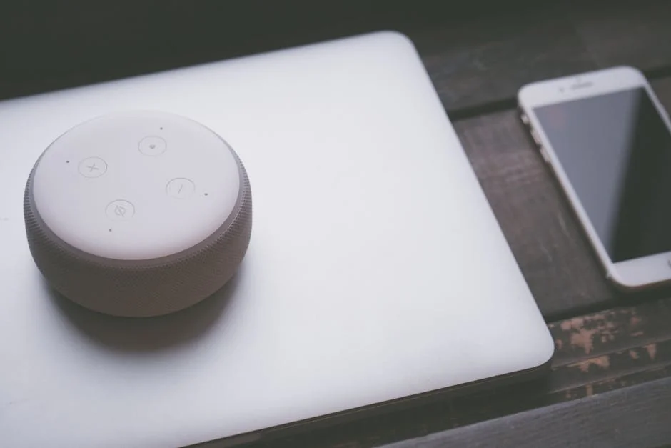 A smart speaker, laptop, and smartphone array representing modern technology lifestyle on a wooden surface. - verified amazon promo codes for electronics